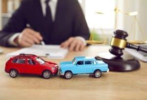 Lawyer with toy cars depicting an accident, gavel and scales of justice on desk.