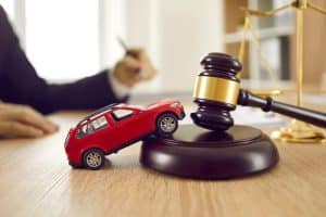 A small red toy car leaning against a judge&rsquo;s gavel, symbolizing a car accident case and legal proceedings.