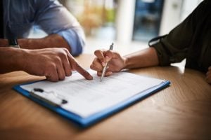 Two people reviewing and signing a document on a clipboard together.