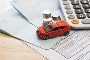 Red toy car on insurance documents with coins and calculator, symbolizing financial planning after accident.