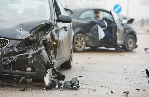 Two cars with severe front-end damage after a collision, debris scattered on the road.