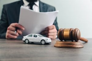 Lawyer reviewing documents with a model car and a gavel on table, symbolizing legal proceedings