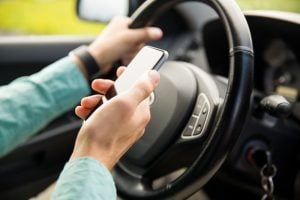 Driver using smartphone while operating vehicle, highlighting a common cause of rideshare accidents.
